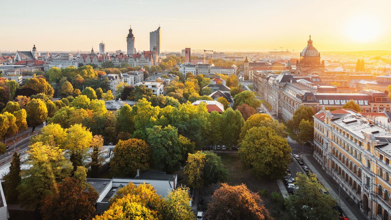 Skyline von Leipzigs Innenstadt bei Sonnenaufgang im Spätsommer, am Horizont sieht man wichtige Sehenswürdigkeiten aus Leipzig wie das City-Hochhaus, das Wintergartenhochhaus und das Bundesverwaltungsgericht